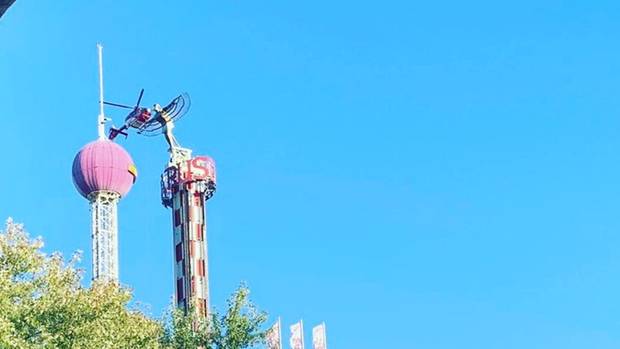 Ein Hubschraiber fliegt neben dem Turm eines Fahrgeschäfts, in dem Menschen festhängen