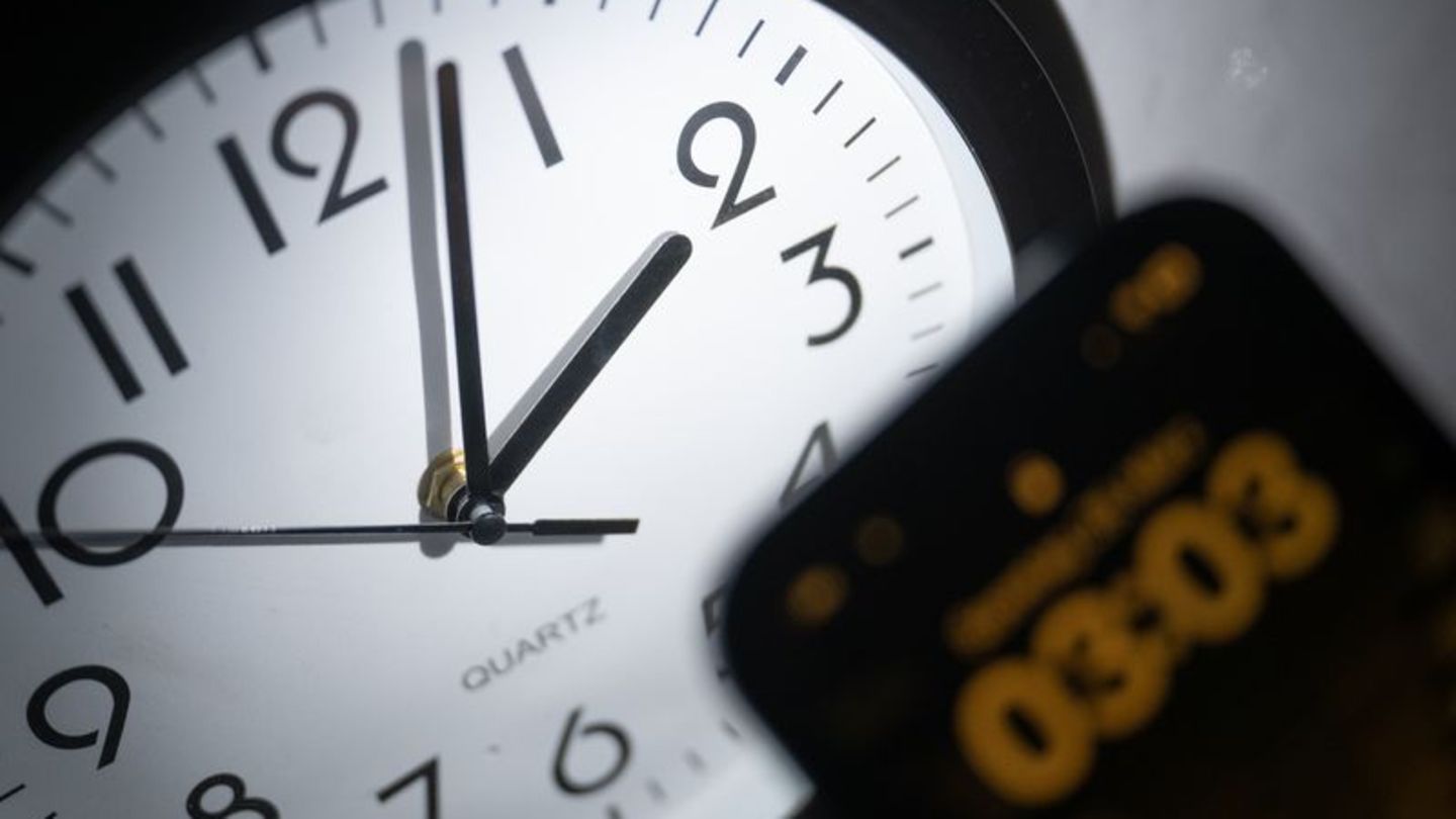 Ein Smartphone zeigt die Uhrzeit "03:03" an, während auf einer analogen Uhr noch 02:03 Uhr ist. Foto: Sebastian Christoph Gollno